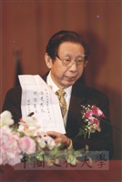 2005年3月1日建校43週年校慶典禮上董事長張鏡湖出示國際歐亞科學院祝賀本校校慶賀詞「源遠流長，根深葉茂」的圖片